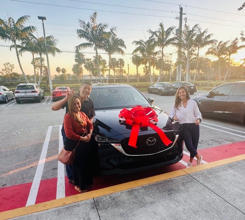 Family celebrating their new Mazda with red bow at sunset
