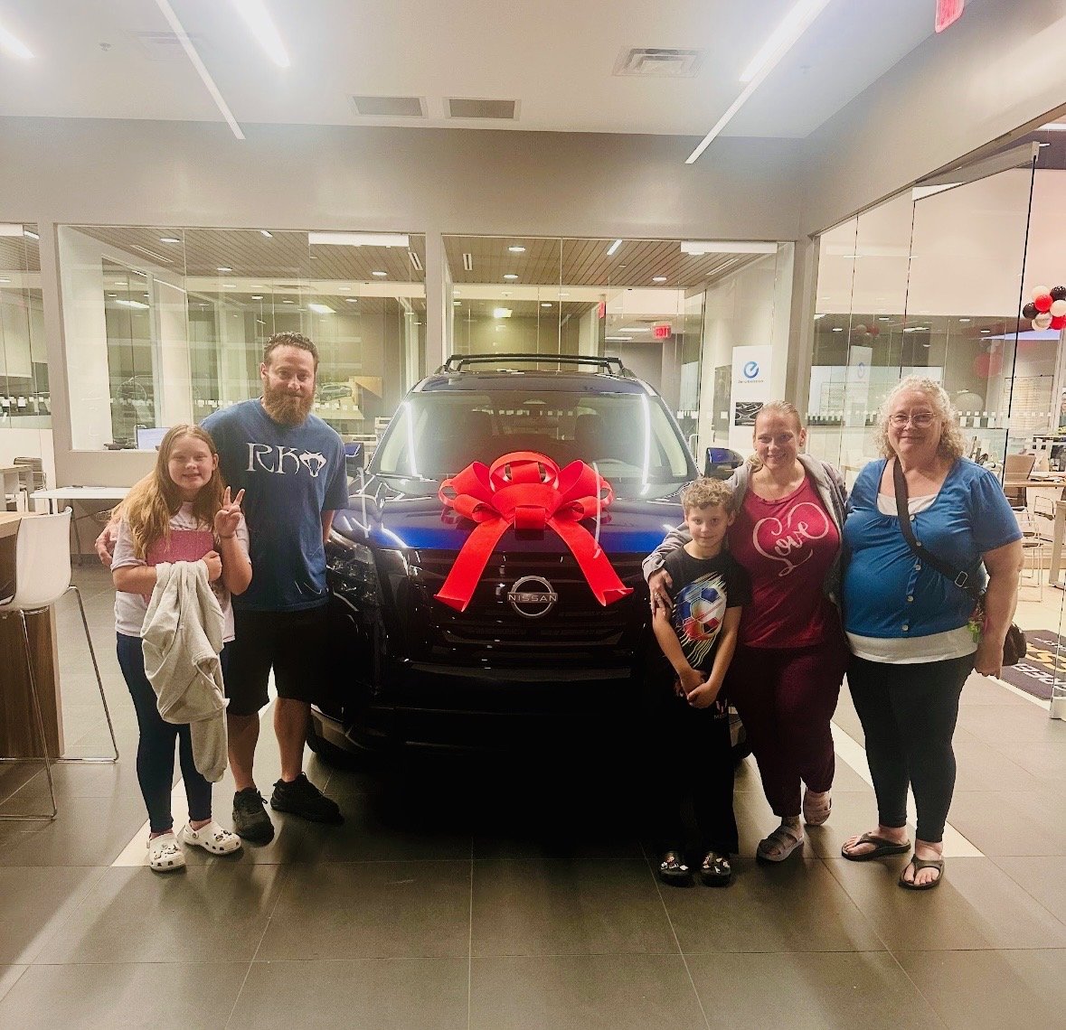 Extended family of five posing with their new blue Nissan inside the showroom