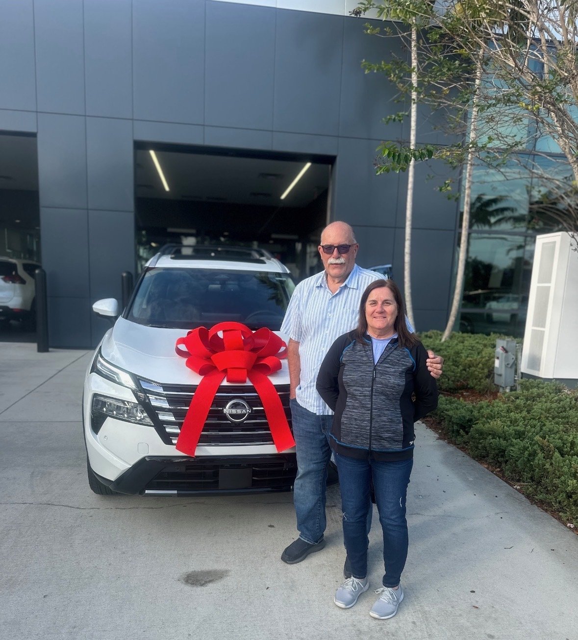 Happy couple with their new white Nissan Rogue with red bow at Palm Beach Nissan